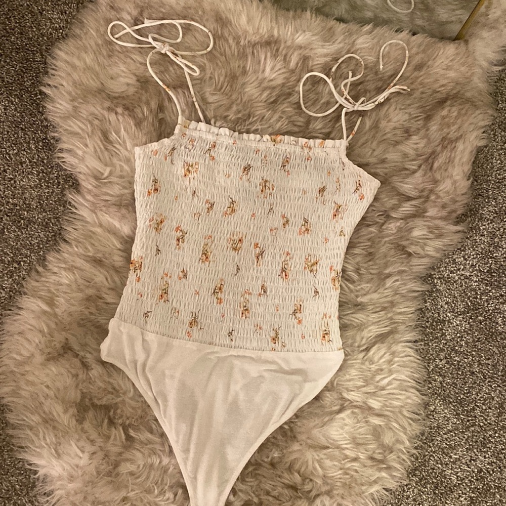 Pleated bodysuit with adjustable straps and a floral pattern on white